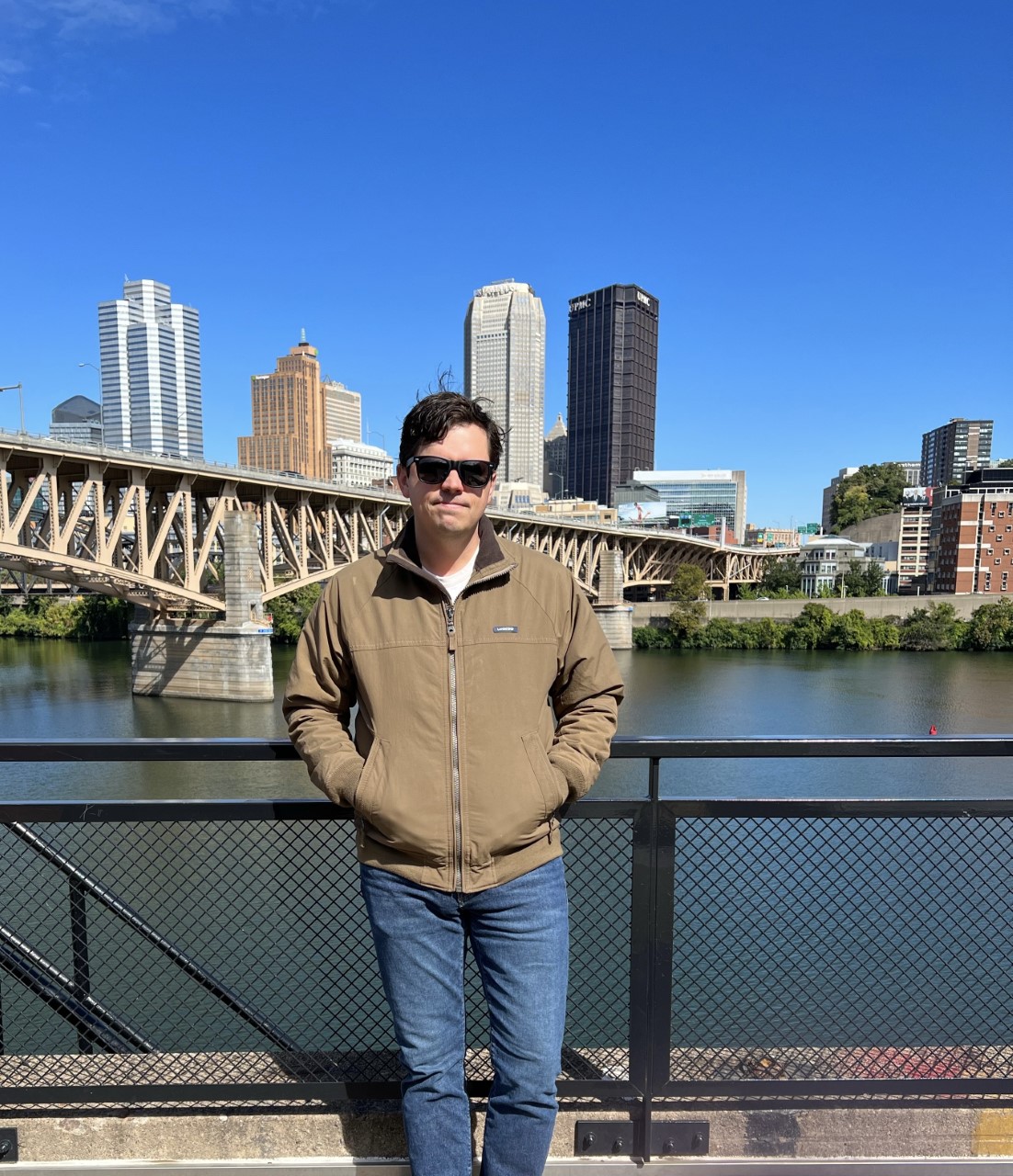 Jon standing on riverside with bridges and downtown pittsburgh in background