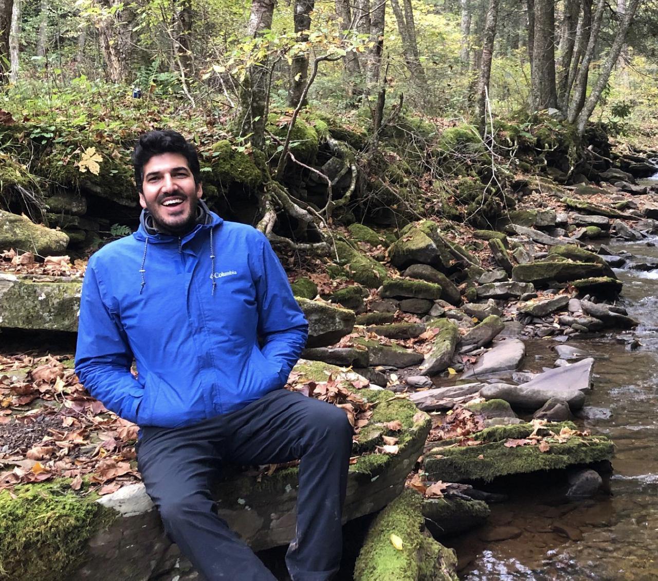 Emrah on rock in the woods near a stream.
